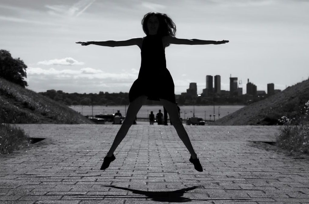 A dynamic black and white silhouette of a woman jumping with arms outstretched in Tallinn, Estonia.